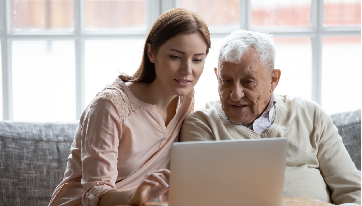 A younger woman assisting an older man on a laptop computer.